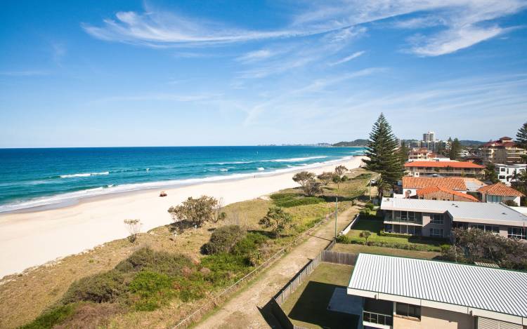 Coastal view of Palm Beach from a high vantage point, showing calm blue waters, white sand, and beachfront houses—ideal for peaceful Queensland getaways.