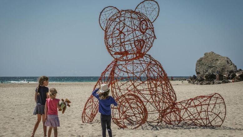 Children admire a giant wire-frame teddy bear sculpture on the beach during Swell Currumbin—an iconic Gold Coast art festival blending creativity and coastal beauty.